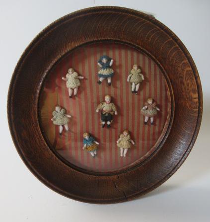 A framed group of eight all bisque doll's house dolls Image