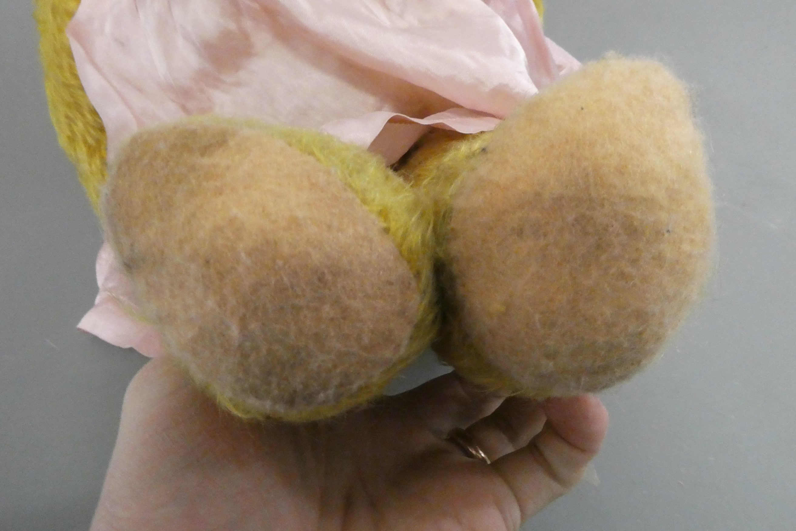 A pre-war teddy bear, with sewn nose, glass amber eyes, blond plush, pink felt pads and pink dress, Image