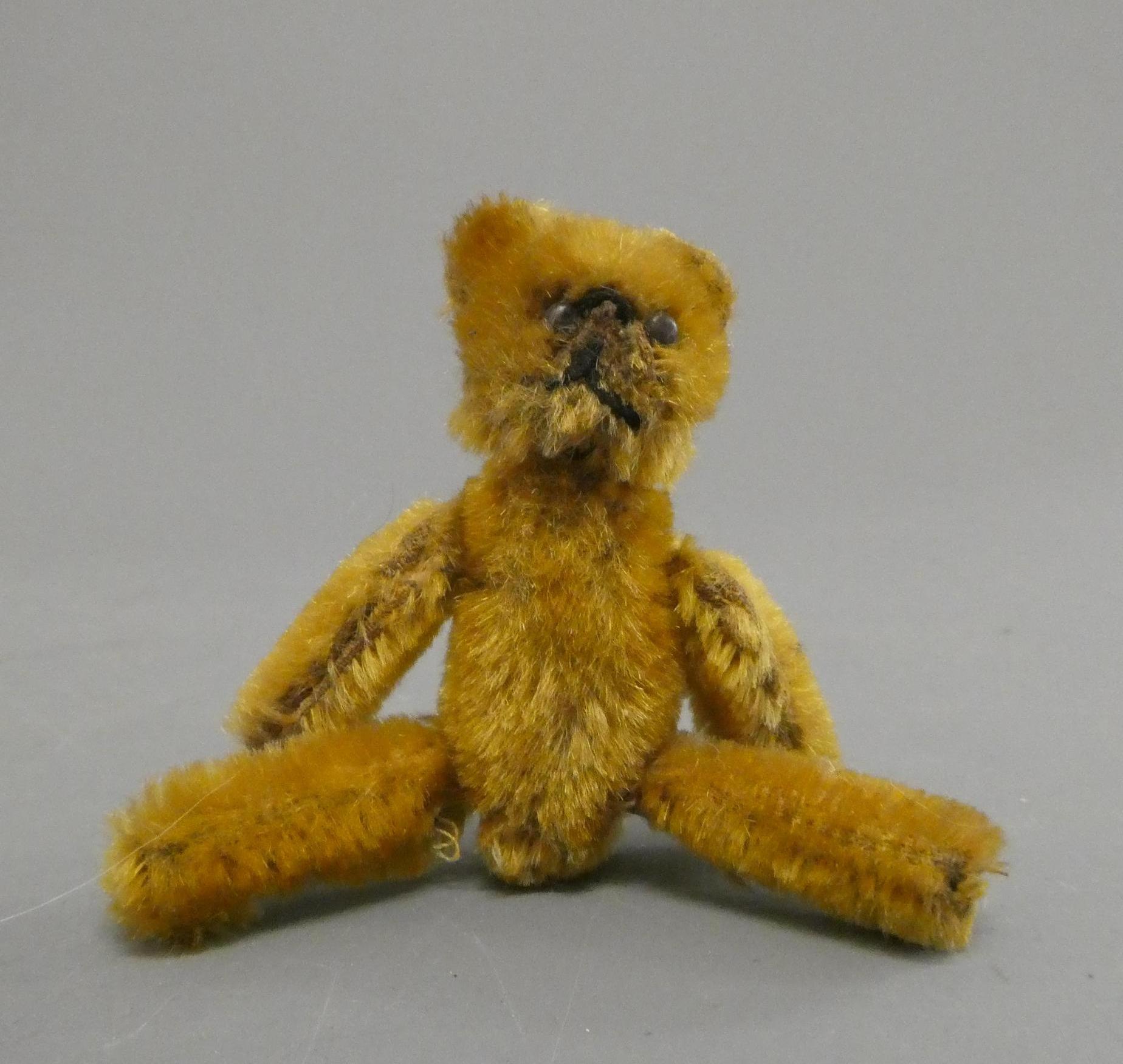 A miniature soldier bear, with black shoe button eyes, sewn mouth, orange plush and jointed Image