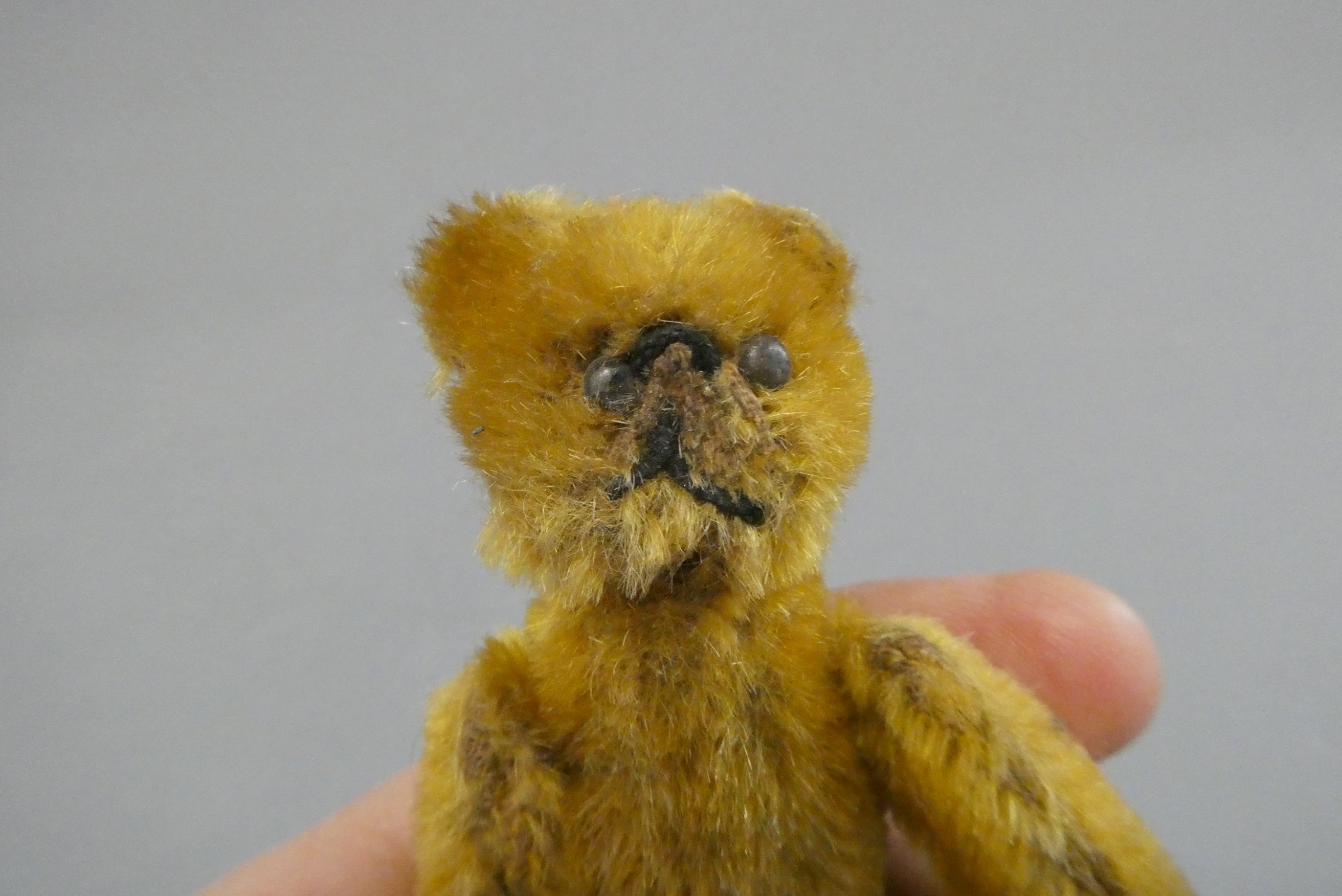 A miniature soldier bear, with black shoe button eyes, sewn mouth, orange plush and jointed Image
