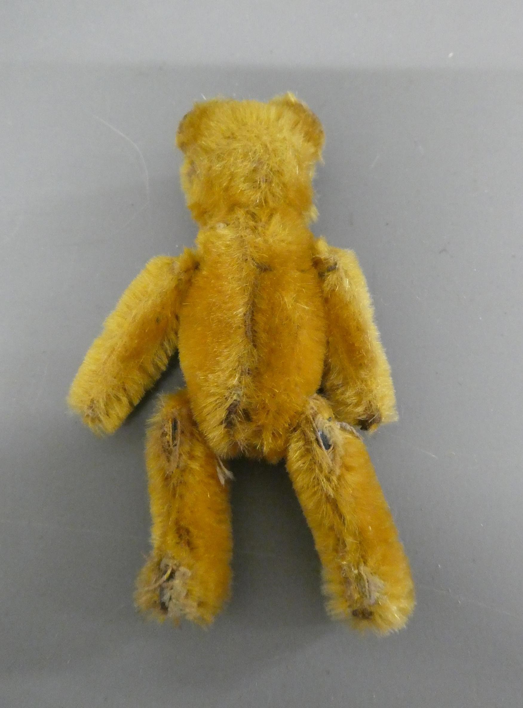 A miniature soldier bear, with black shoe button eyes, sewn mouth, orange plush and jointed Image