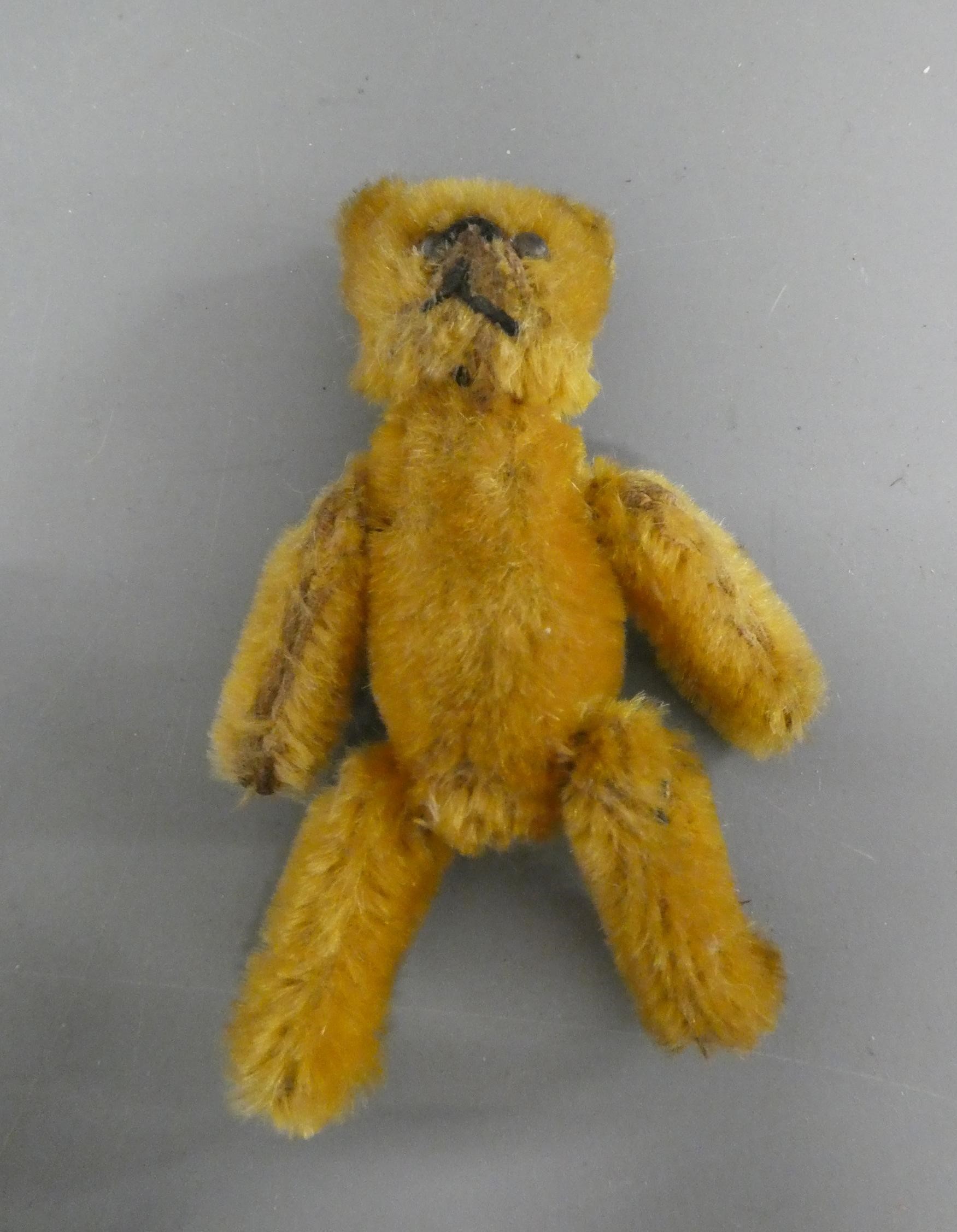 A miniature soldier bear, with black shoe button eyes, sewn mouth, orange plush and jointed Image
