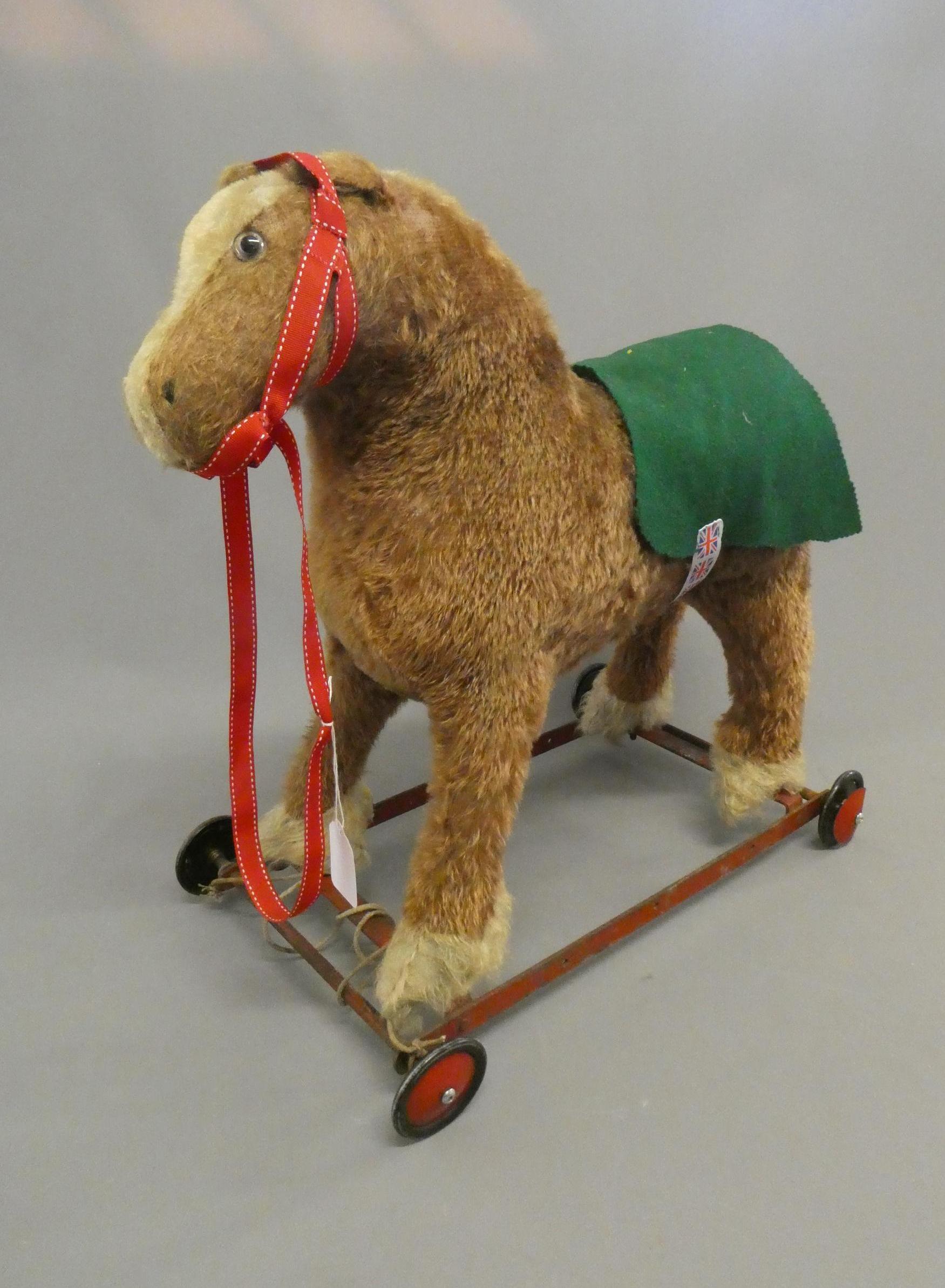 A vintage plush pull-a-long horse, with clear glass eyes and red metal frame with four wheels, 20" x Image