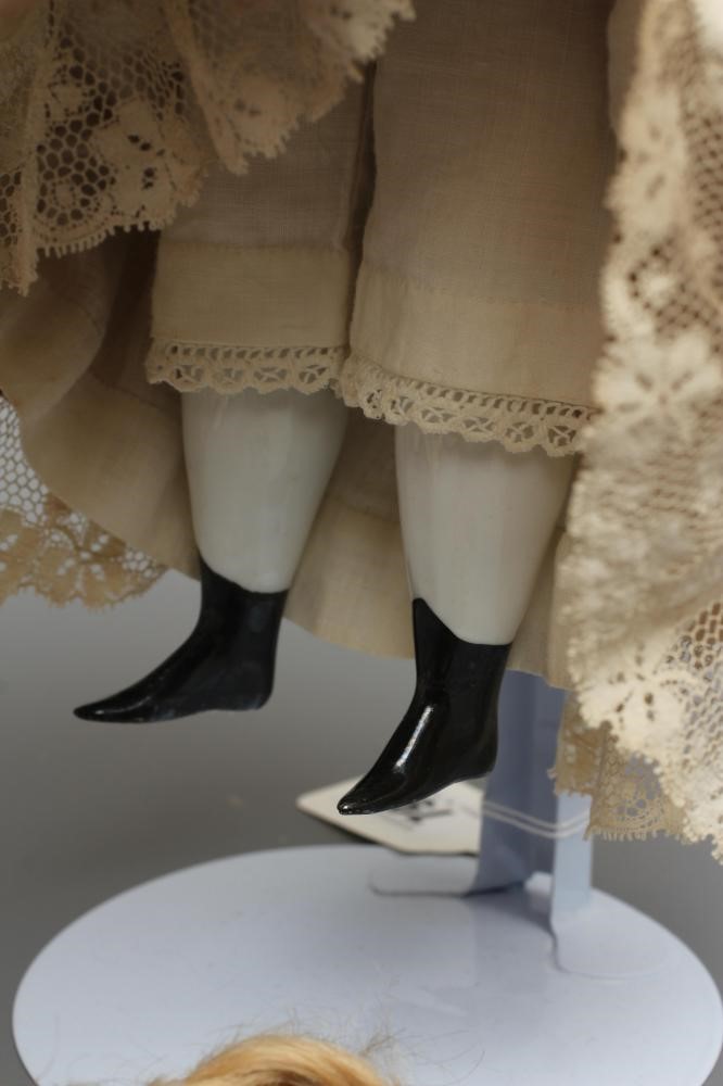 A Victorian china shoulder head doll, with painted face, blond wig, fabric body, china lower limbs Image