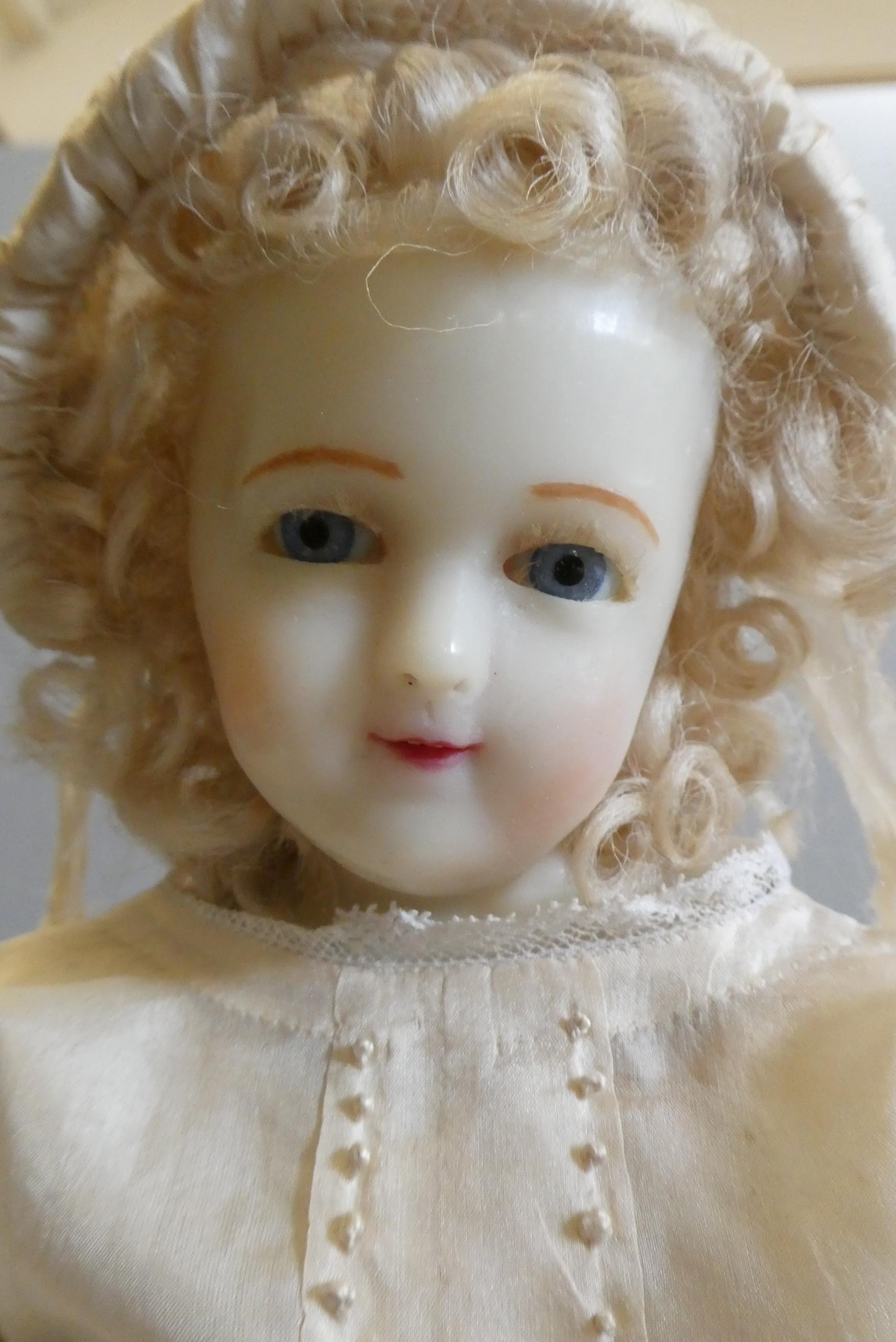 A seated wax shoulder head doll, with blue glass fixed eyes, open mouth, teeth, blond wig, fabric Image