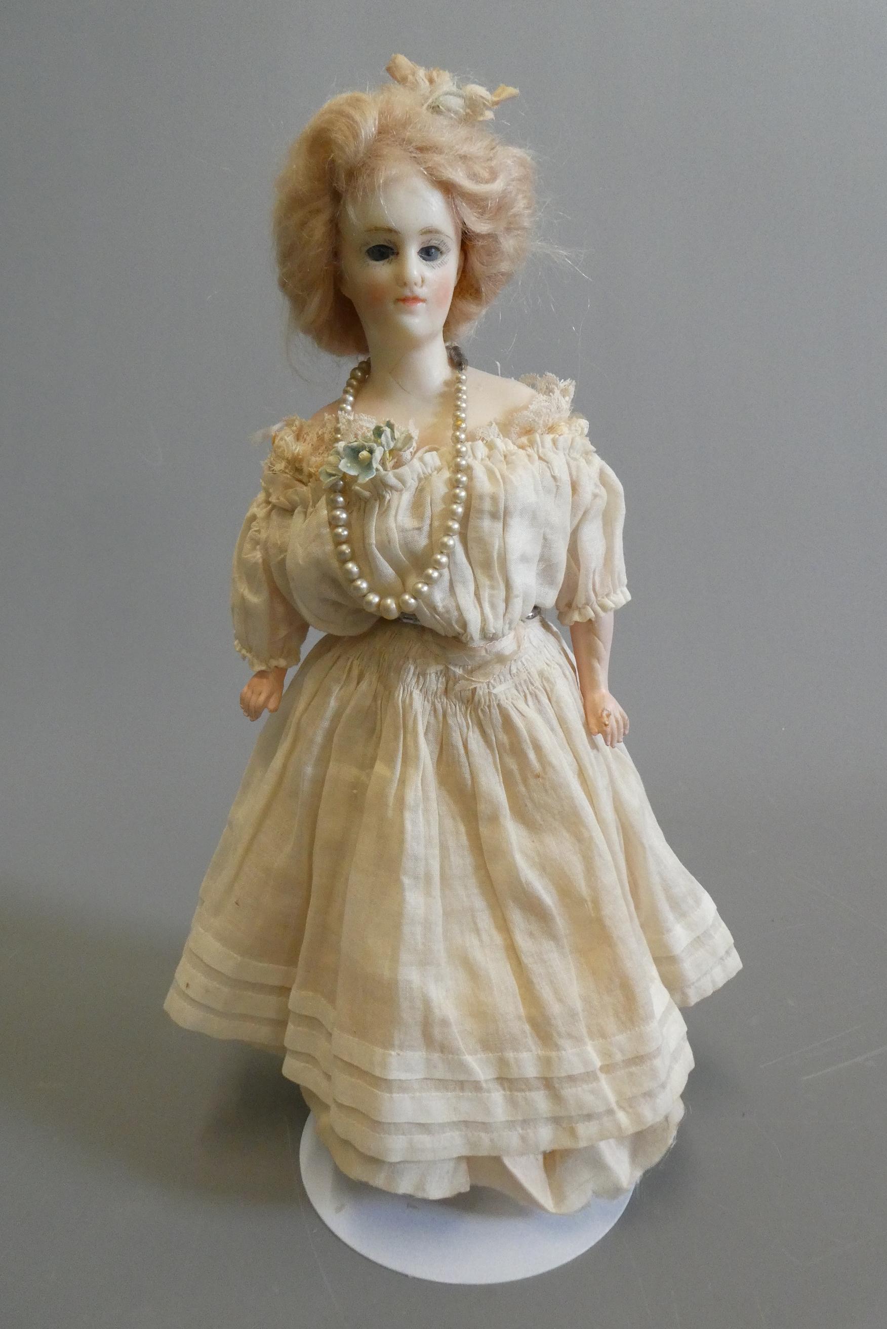 A late Victorian wax shoulder head doll, with blue glass fixed eyes, closed mouth, blond wig, fabric Image