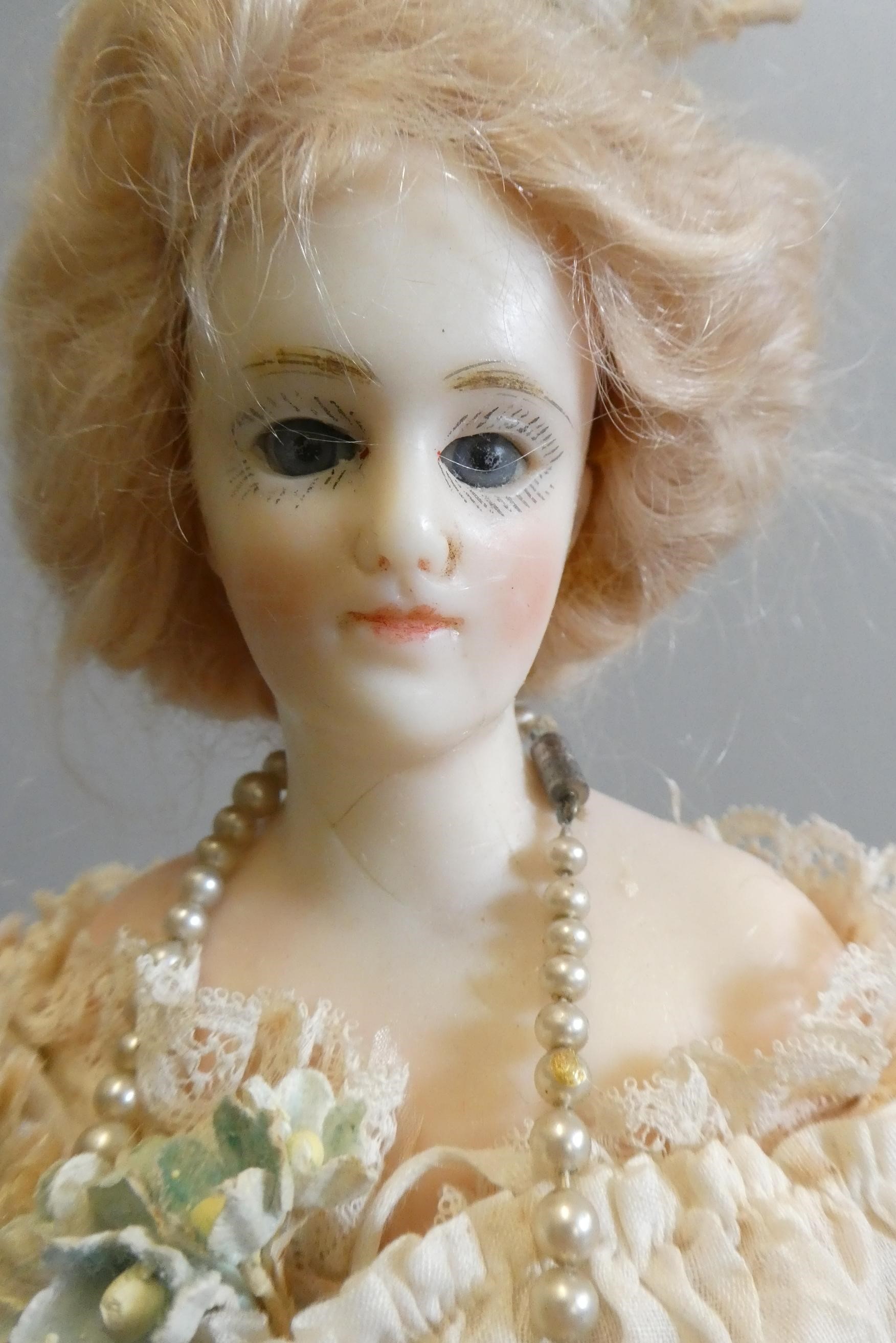 A late Victorian wax shoulder head doll, with blue glass fixed eyes, closed mouth, blond wig, fabric Image