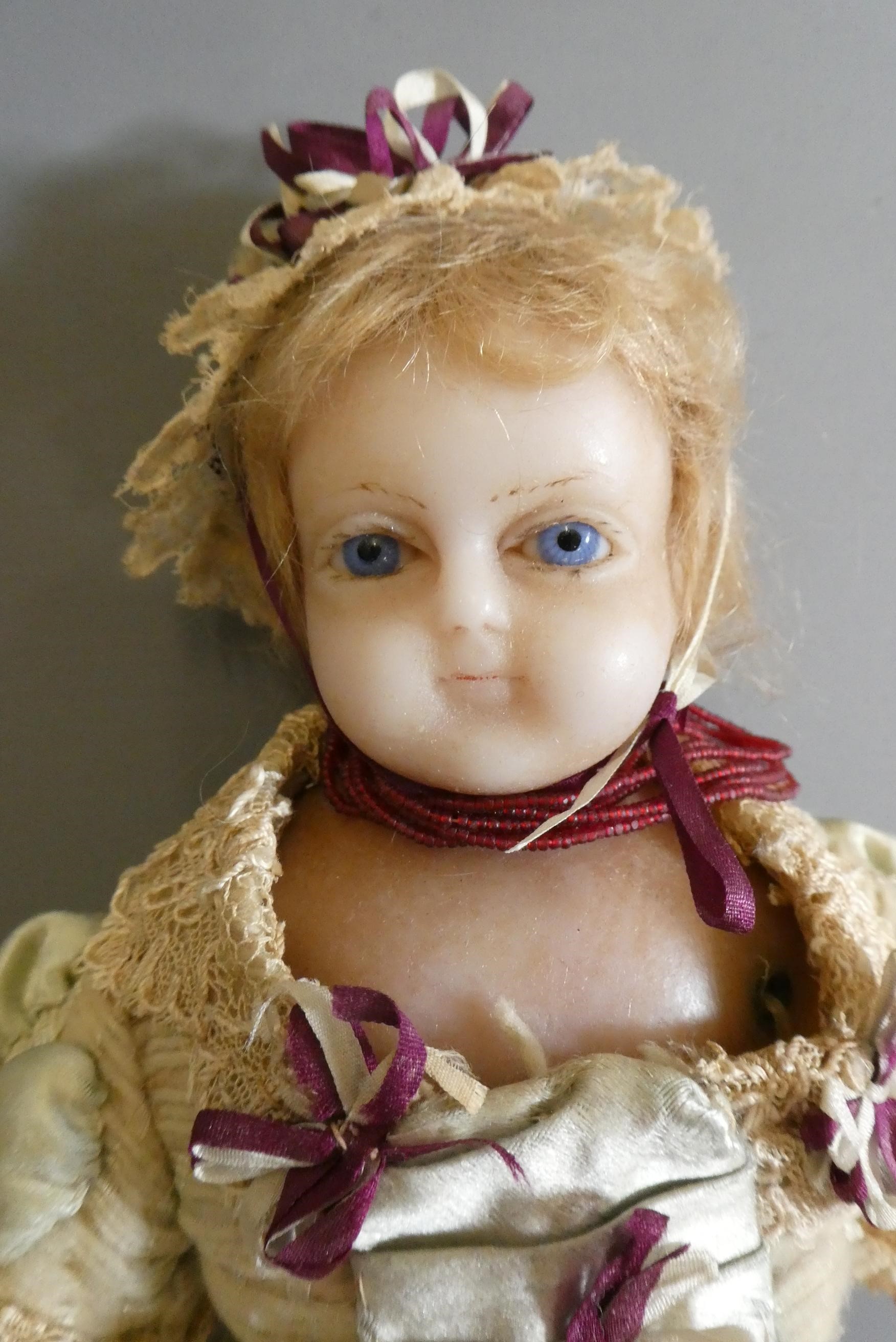 A Victorian wax shoulder head doll, with blue glass fixed eyes, closed mouth, blond wig, fabric Image