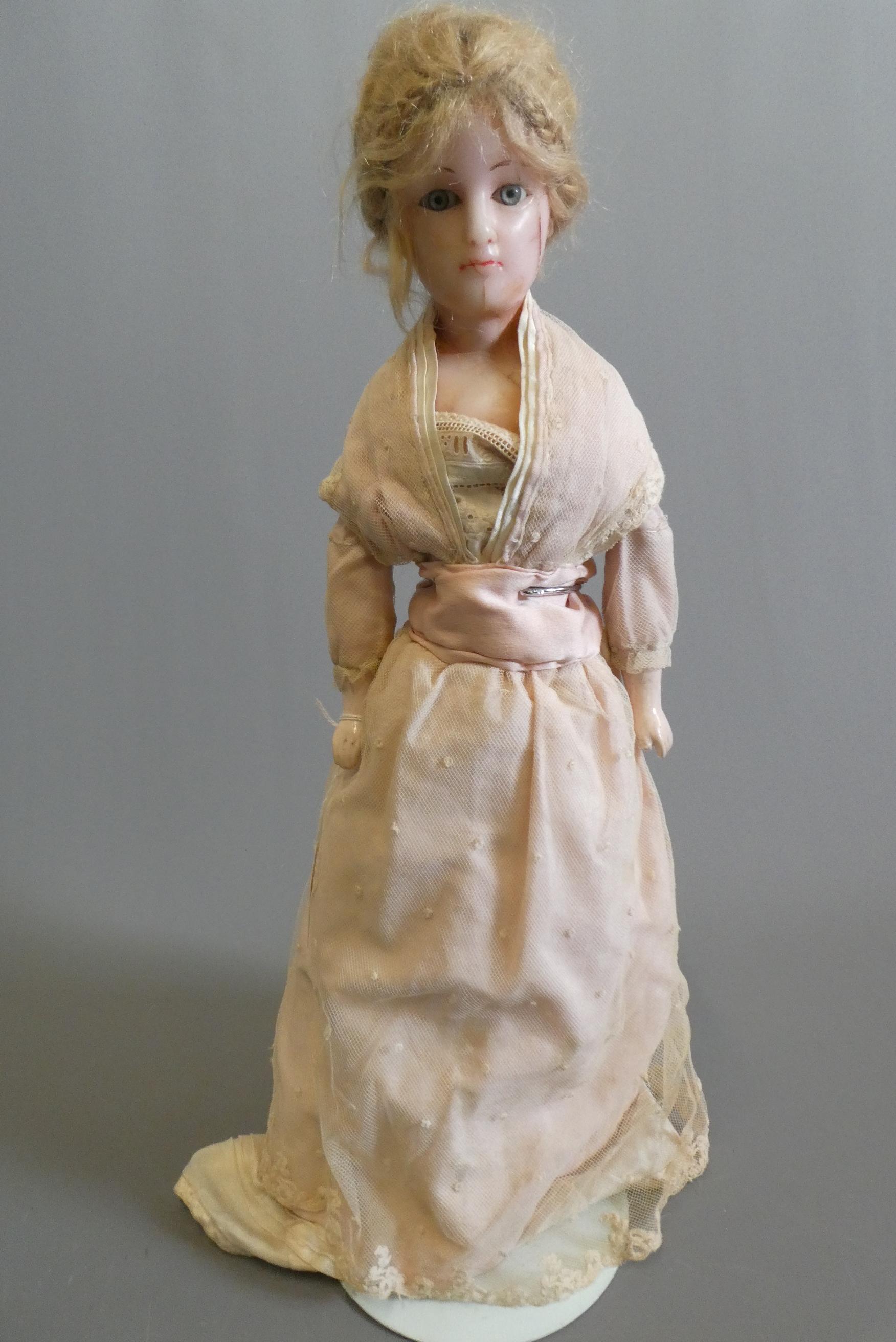 A late Victorian wax shoulder head doll, with blue glass fixed eyes, closed mouth, blond wig, fabric Image