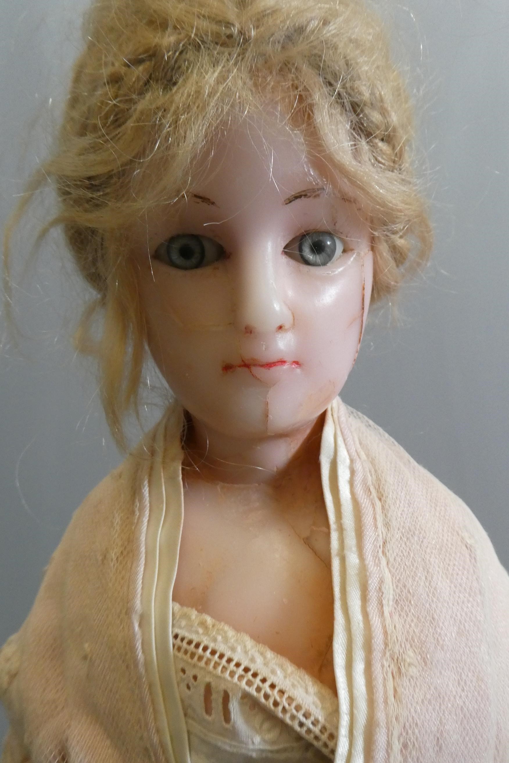 A late Victorian wax shoulder head doll, with blue glass fixed eyes, closed mouth, blond wig, fabric Image