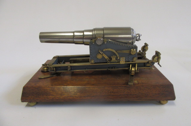 A model cannon in steel with brass fittings comprising 9" cannon on wheeled base mounted on oak Image