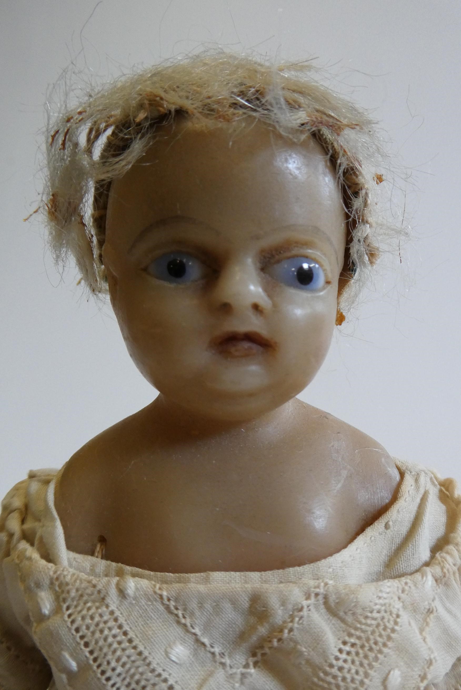 A Victorian wax shoulder head doll with blue glass fixed eyes, moulded open mouth, blond wig, fabric Image