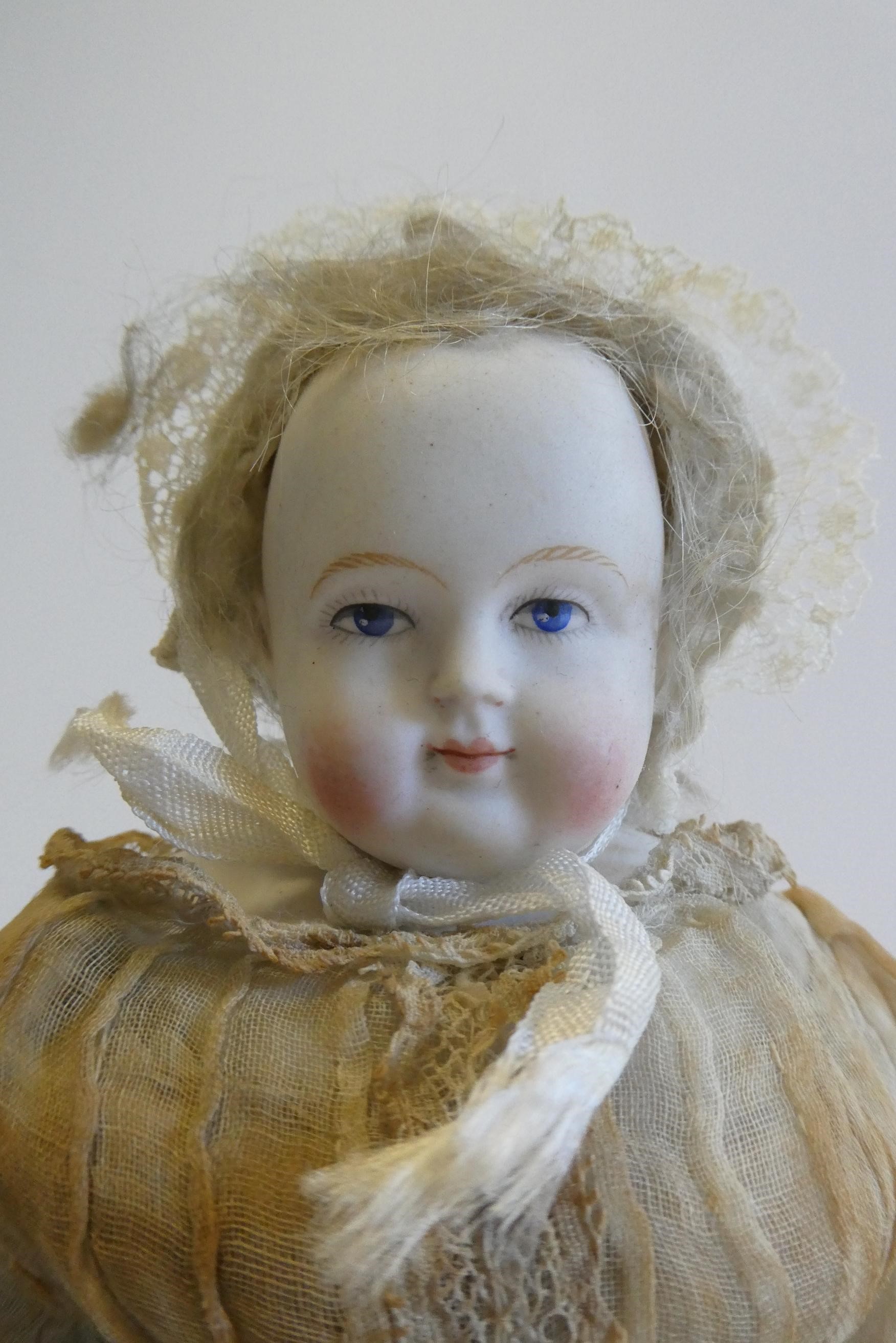 A bisque shoulder head doll, 19th century, with painted features, blond wig, fabric body and china Image