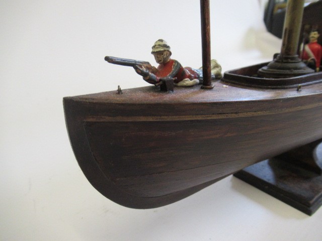 A modern wooden model of a steam launch and four lead figures with flag Image