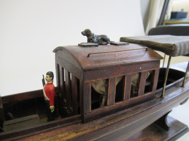 A modern wooden model of a steam launch and four lead figures with flag Image