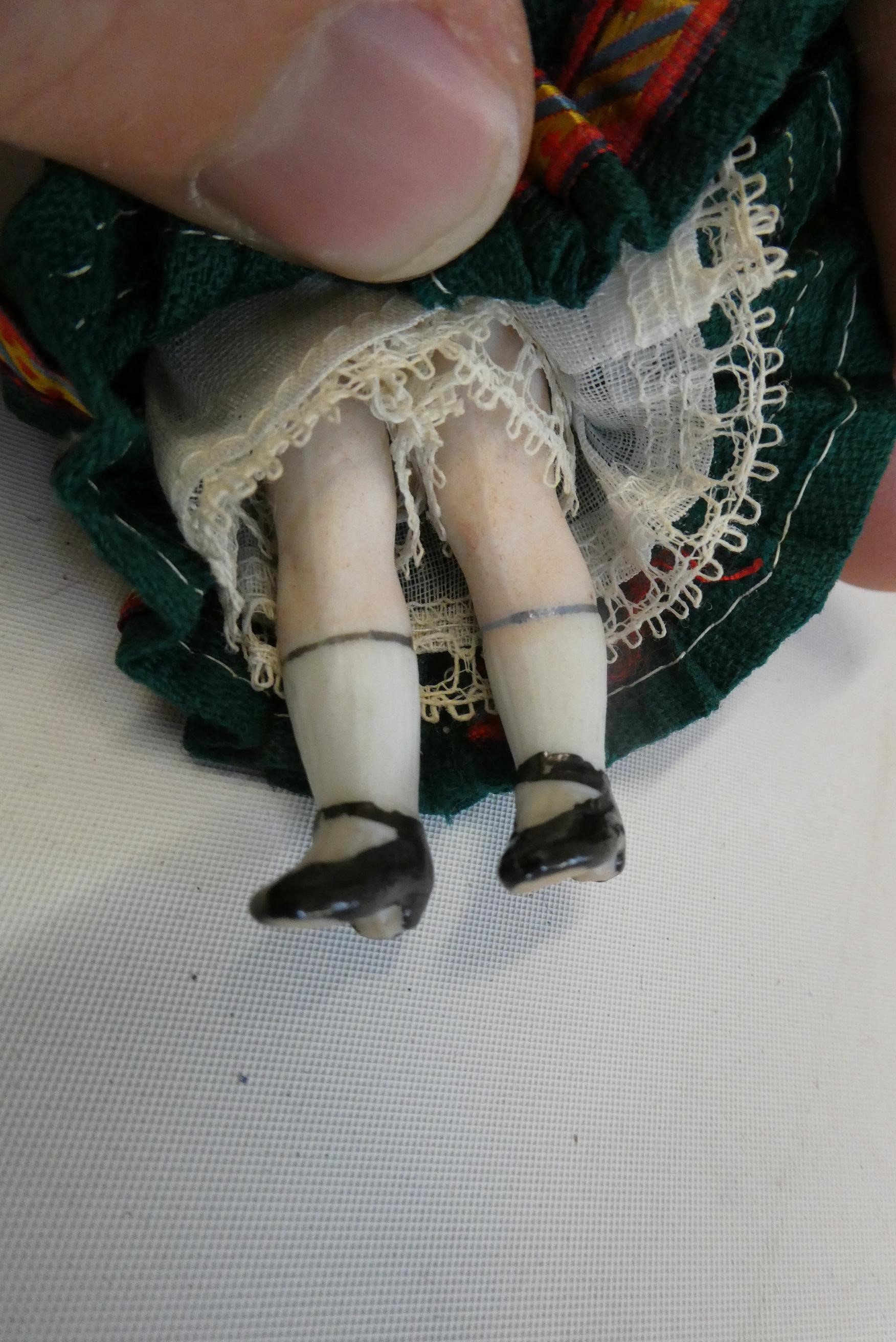 An all bisque dolls house doll, with brown glass fixed eyes, blond wig, straight legs, moulded shoes Image