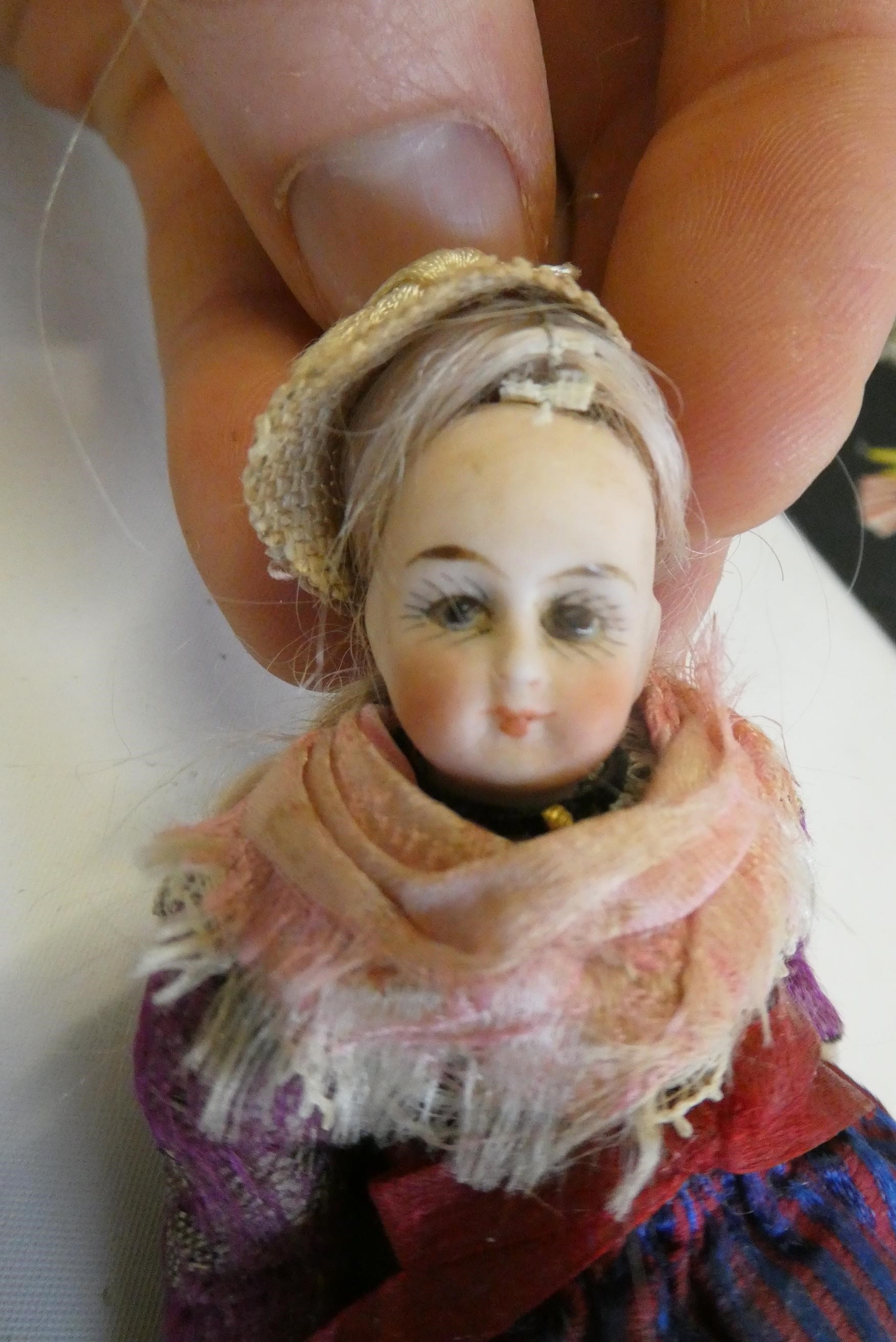 An all bisque dolls house doll, with brown glass fixed eyes, blond wig, straight legs, moulded shoes Image