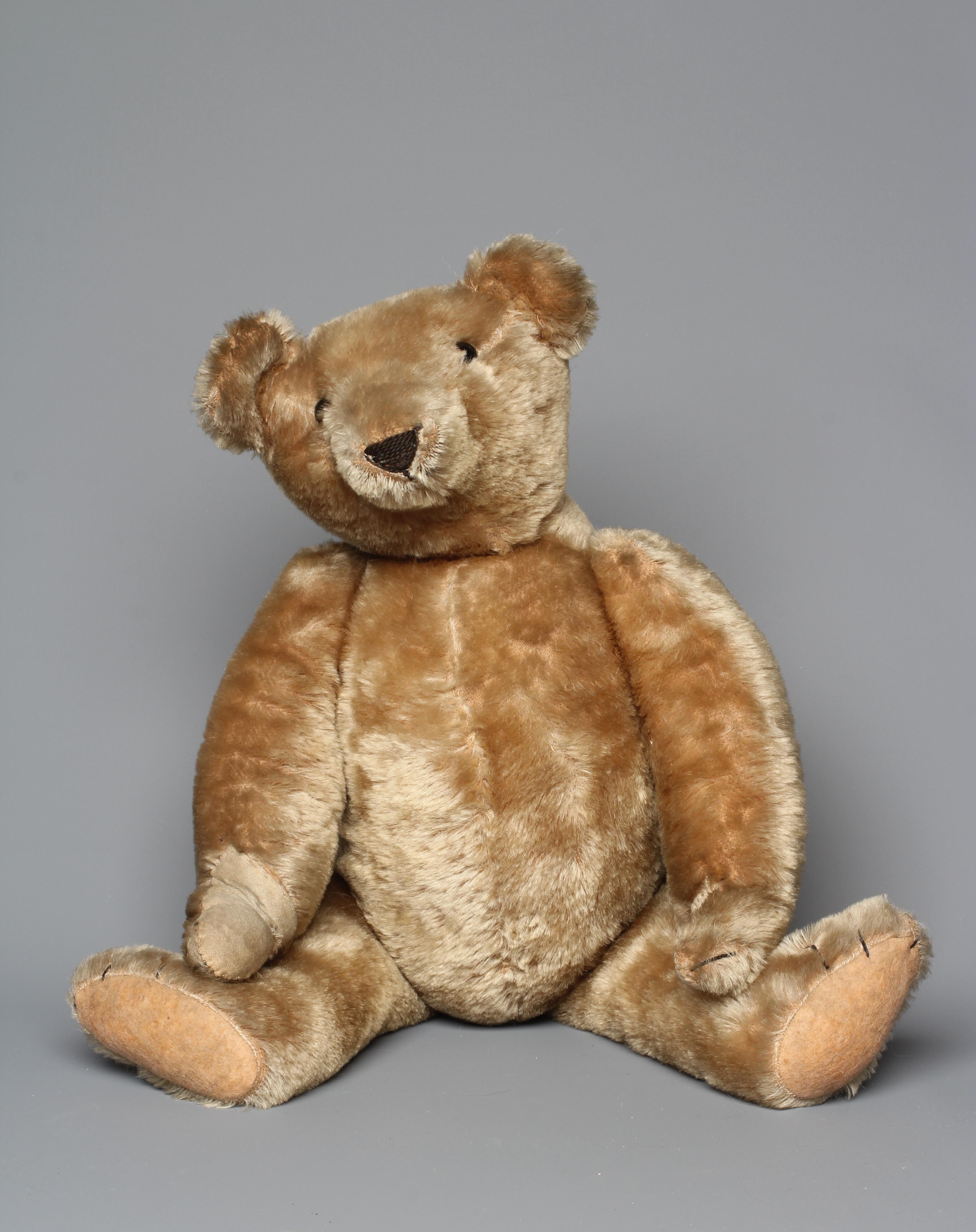 An early teddy bear, circa 1920, with shoe button eyes, sewn nose, long snout, back hump, Image