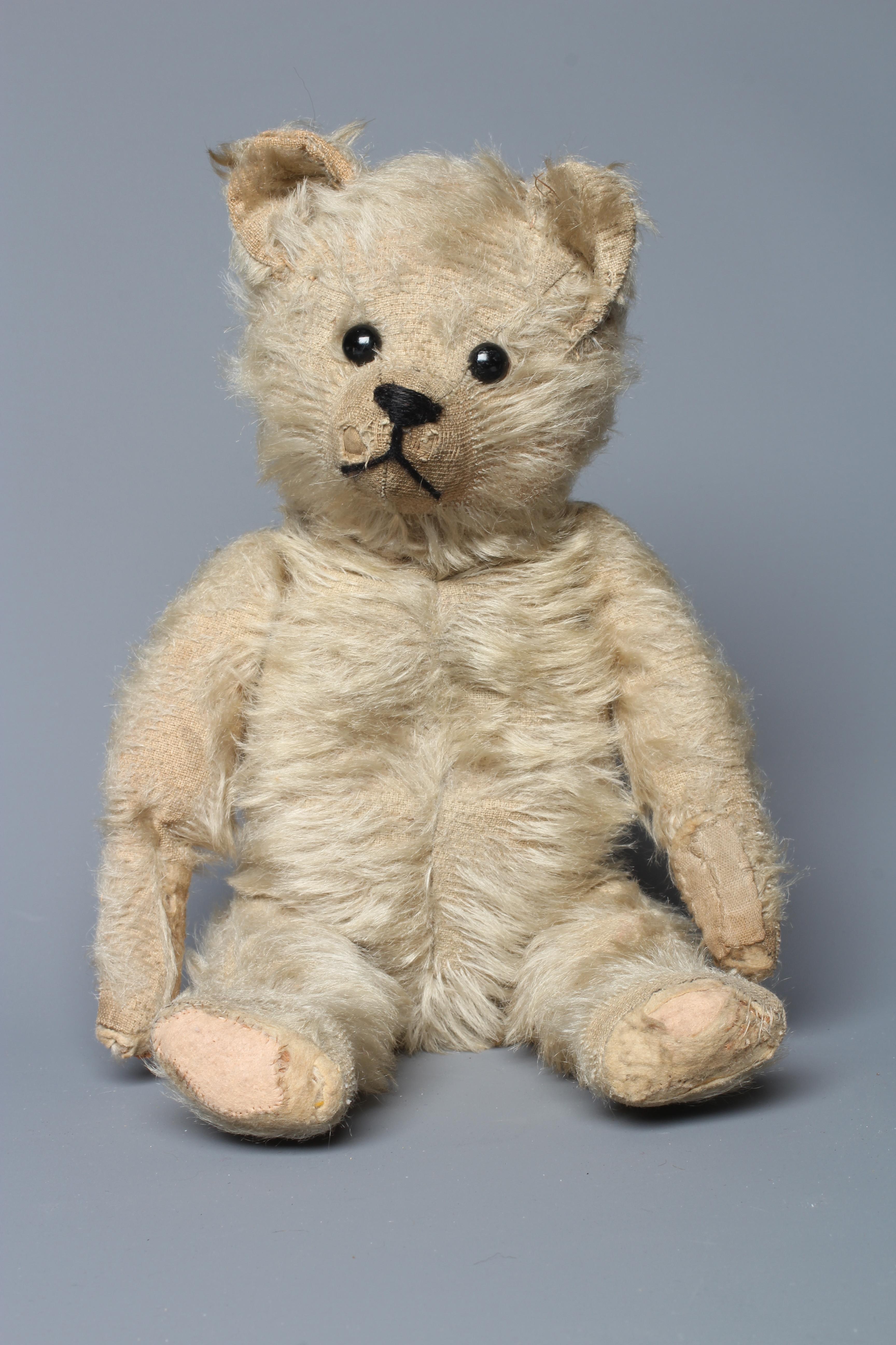 An antique straw filled teddy bear, with black shoe button eyes, sewn nose and light plush, 14" long Image