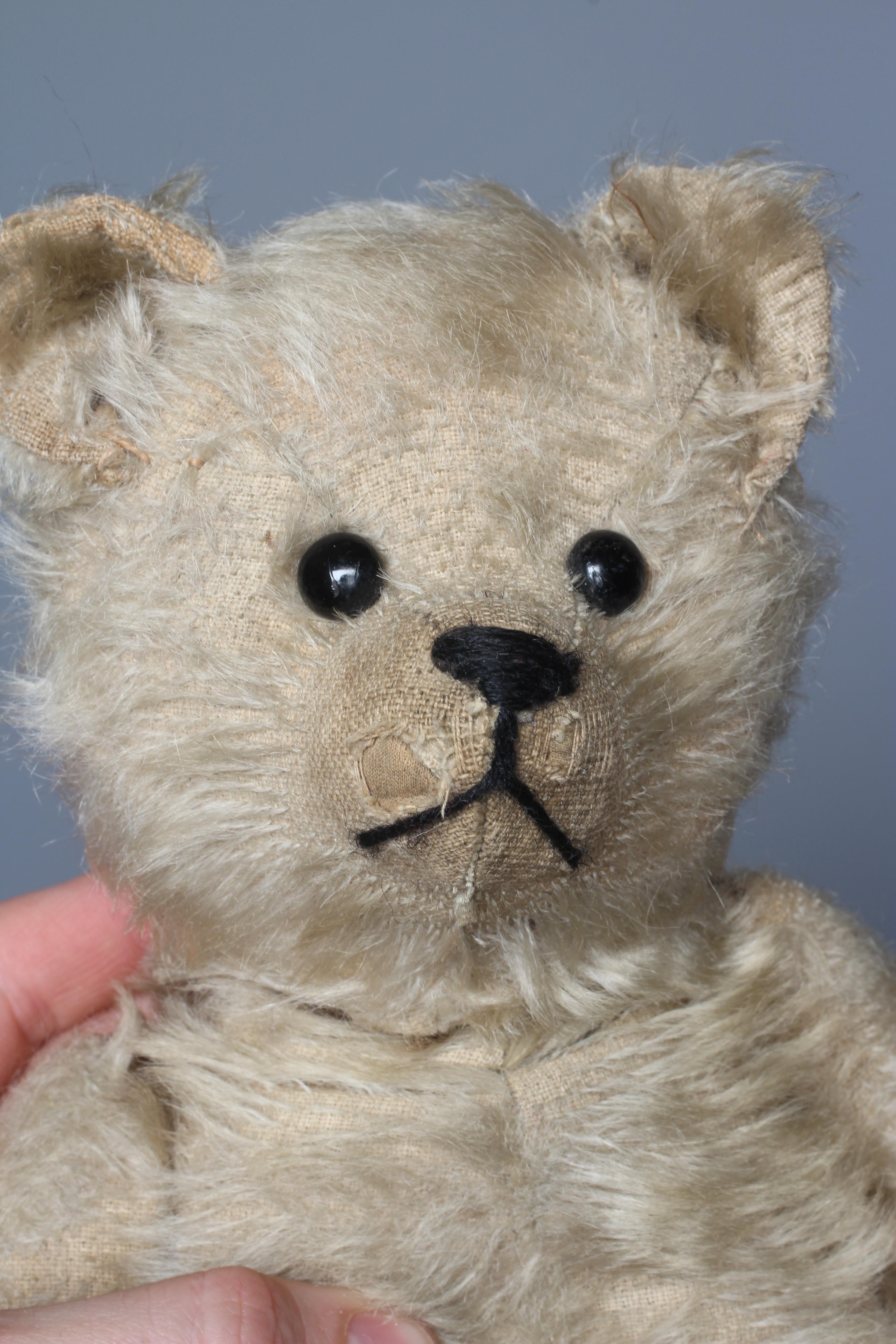 An antique straw filled teddy bear, with black shoe button eyes, sewn nose and light plush, 14" long Image
