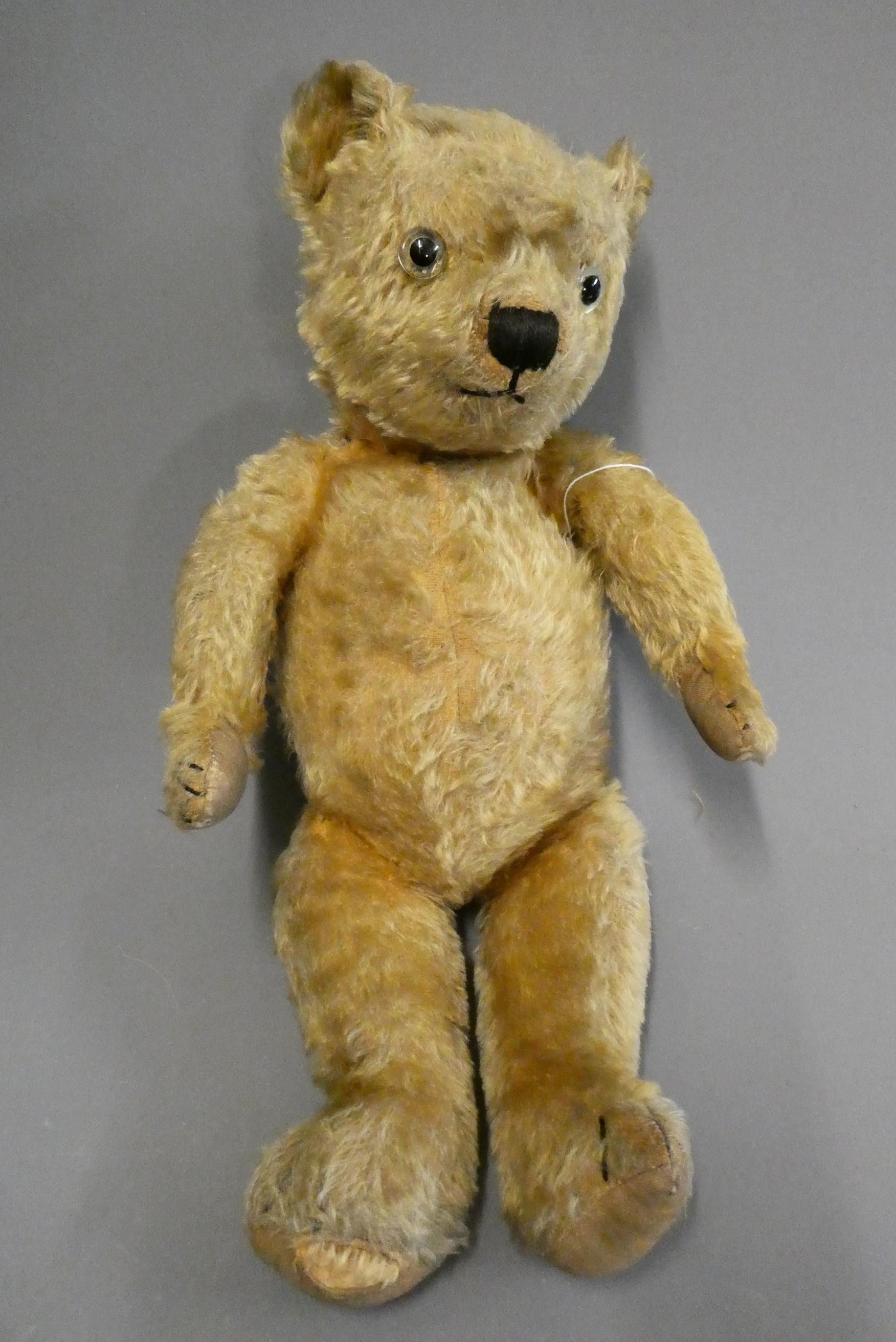 An English teddy bear, possibly Chiltern, with clear glass eyes, sewn nose, jointed body and fabric Image