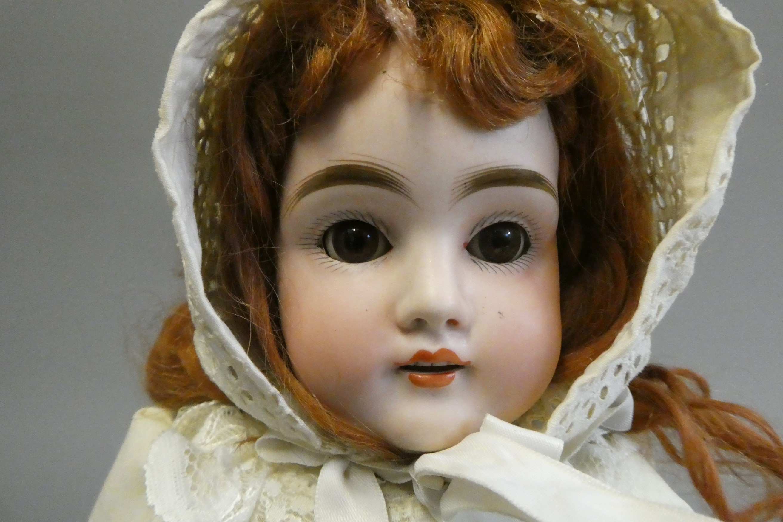 A bisque shoulder head doll, with brown glass sleeping eyes, open mouth, teeth, auburn wig, kid Image