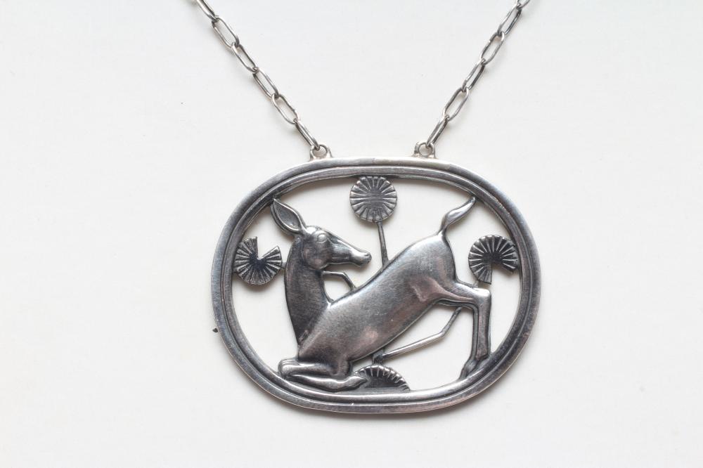 A GEORG JENSEN SILVER OVAL PENDANT designed by Arno Malinowski with a kneeling deer amongst flowers, Image