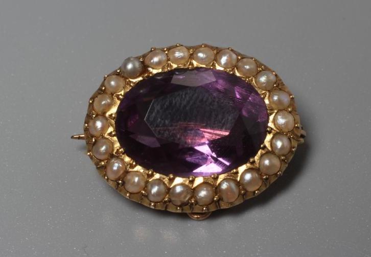 A LATE VICTORIAN OVAL AMETHYST BROOCH centred by a facet cut stone within a border of seed pearls to Image