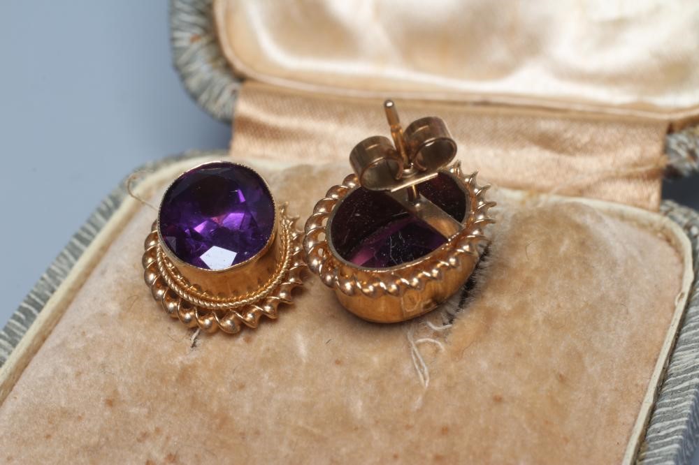 A PAIR OF AMETHYST EAR STUDS, the oval facet cut stones in deep collets with twisted borders to Image