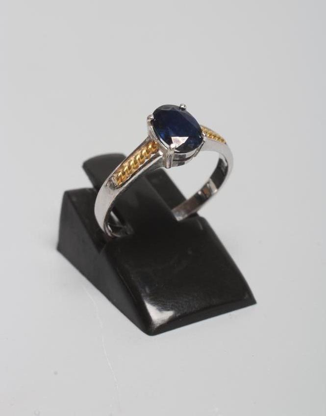 A SOLITAIRE SAPPHIRE RING, the oval facet cut stone claw set to yellow rope twist set shoulders and Image