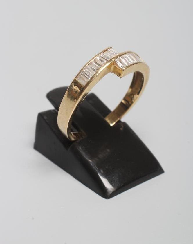 A MODERN DIAMOND CROSSOVER RING, the eighteen baguette cut stones channel set to a plain shank Image