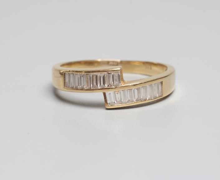 A MODERN DIAMOND CROSSOVER RING, the eighteen baguette cut stones channel set to a plain shank Image