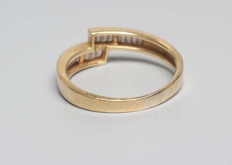 A MODERN DIAMOND CROSSOVER RING, the eighteen baguette cut stones channel set to a plain shank Image