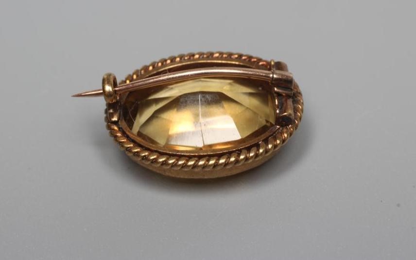AN OVAL CITRINE SMALL BROOCH, the facet cut stone collet set to an unmarked rope twist frame (Est. Image