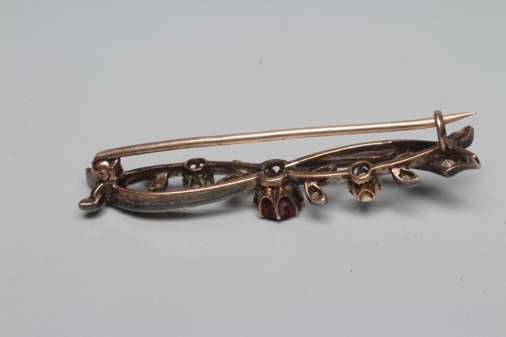 A LATE VICTORIAN BROOCH centred by a facet cut ruby claw set to scrolls set with small diamonds and Image