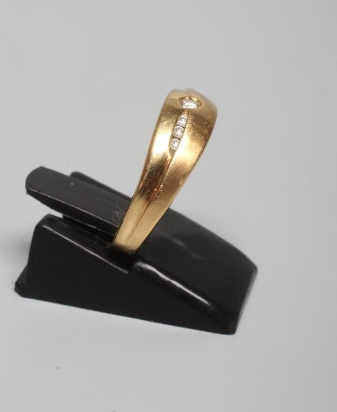 A DIAMOND RING with a single small stone in rub-over setting beside three smaller channel set stones Image