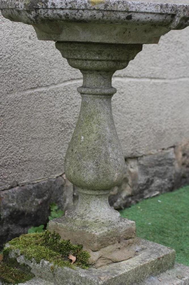 A CAST STONE BIRD BATH, the shallow circular bowl raised on turned baluster stem and stepped square Image