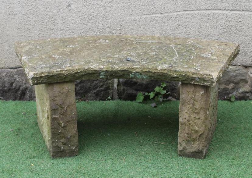 A SANDSTONE BENCH of crescent form with rough hewn edges, raised on oblong end supports, 45" w x 18 Image