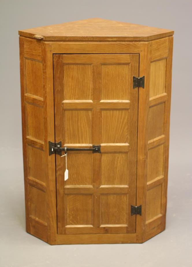 PETER HEAP OF WETWANG - AN ADZED OAK CORNER CUPBOARD of canted multi-panel form with moulded edged Image