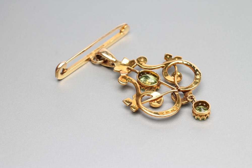 AN EDWARDIAN 9CT GOLD PENDANT of open shield form set with two facet cut peridots and split seed Image