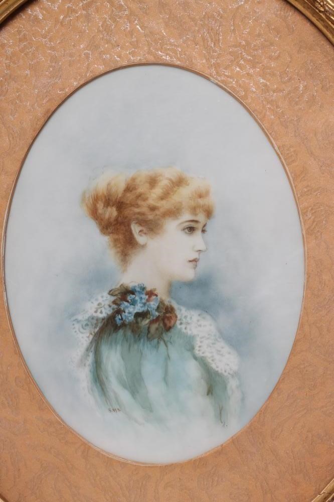 AN EDWARDIAN OPAQUE GLASS OVAL PANEL painted with the half length portrait of a young lady wearing a Image