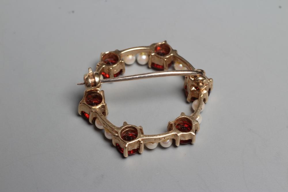 A GARNET AND SEED PEARL CIRCLET BROOCH claw set with six facet cut garnets and twelve pearls to a Image