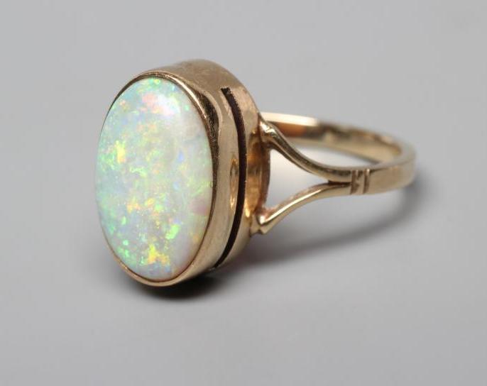 AN OPAL DRESS RING, the oval cabochon polished stone collet set to open shoulders and a plain 9ct Image