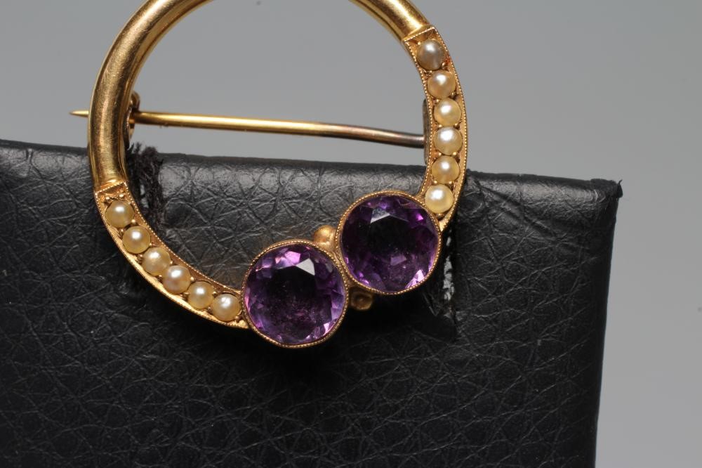 AN EDWARDIAN CIRCLET BROOCH, the hollow frame collet set with two facet cut amethysts within borders Image