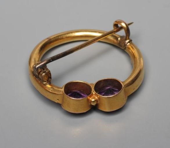 AN EDWARDIAN CIRCLET BROOCH, the hollow frame collet set with two facet cut amethysts within borders Image