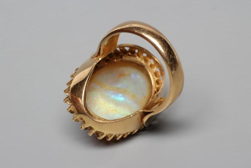 AN OPAL DRESS RING, the oval cabochon polished stone collet set to a border of numerous small Image