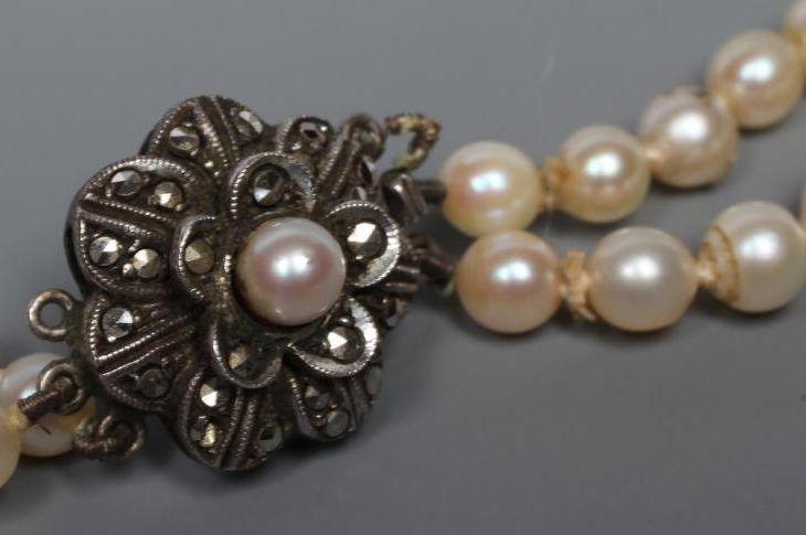 A DOUBLE STRAND OF CULTURED PEARLS with marcasite set silver flower clasp, stamped 935 (Est. plus Image