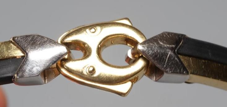 A BARAKA STIFF HINGED BANGLE, the bi-coloured metal stamped 750, with black rubber sections tied by Image