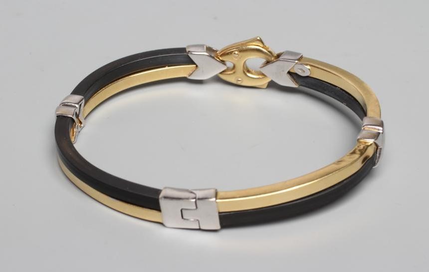 A BARAKA STIFF HINGED BANGLE, the bi-coloured metal stamped 750, with black rubber sections tied by Image