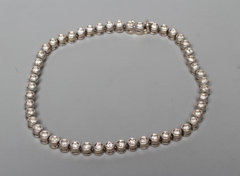 A DIAMOND TENNIS BRACELET, the fifty small round brilliants collet set to a plain white frame Image